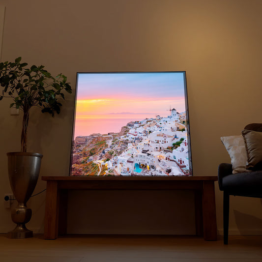 LED-Bild mit schwarzem Rahmen, Blick auf weißen Ort und Meer bei Sonnenuntergang