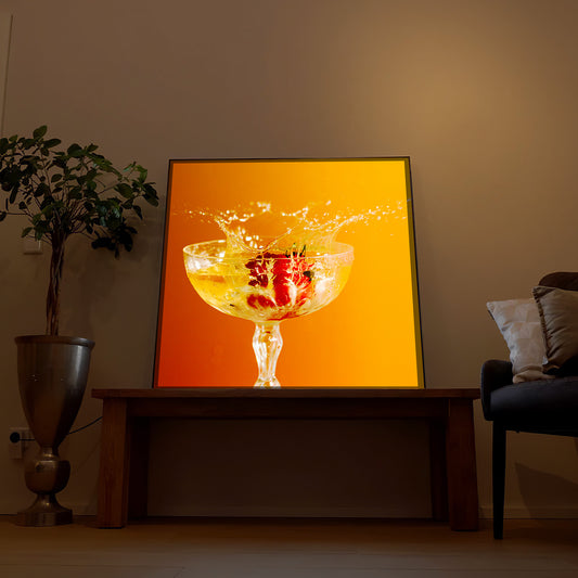 Gerahmtes LED-Bild mit Glas Orangensaft und Spritzern auf orangefarbenem Hintergrund