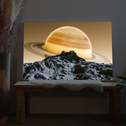 LED-Bild im schwarzen Rahmen: leuchtender Saturn über felsigem Gebirge